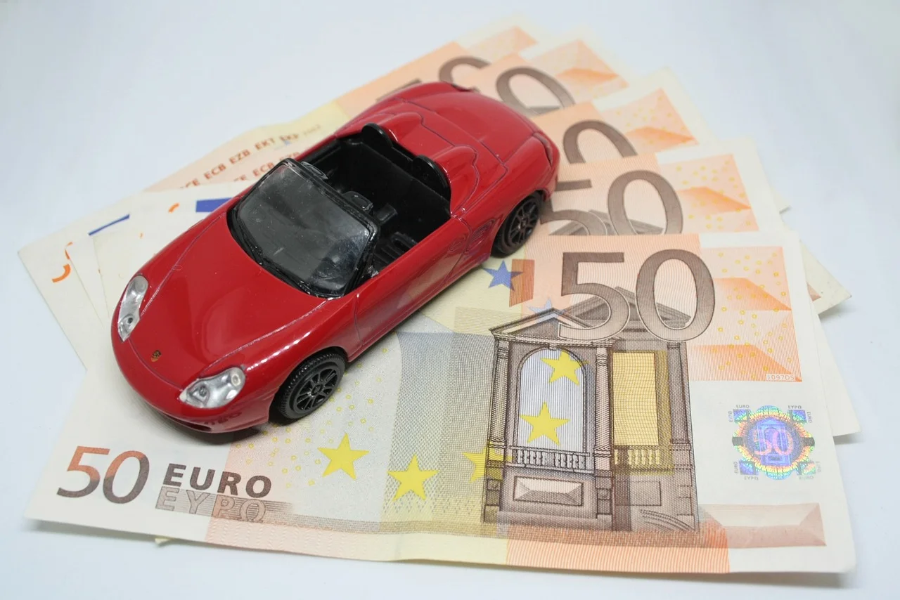 Czerwony samochód na banknotach 50 euro, symbol kosztów leasingu i ubezpieczenia auta